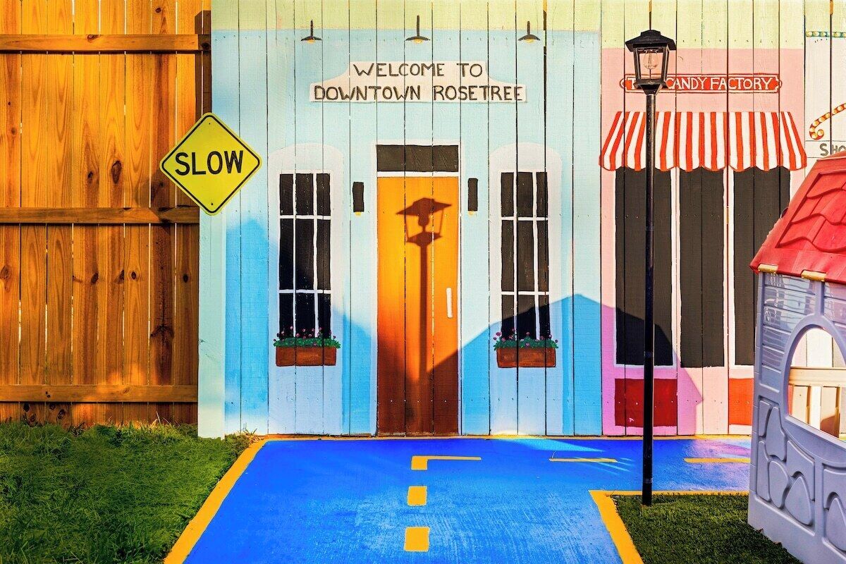 A colorful building with a 'SLOW' sign, a 'WELCOME TO DOWNTOWN ROSETREE' sign, and a candy factory sign.