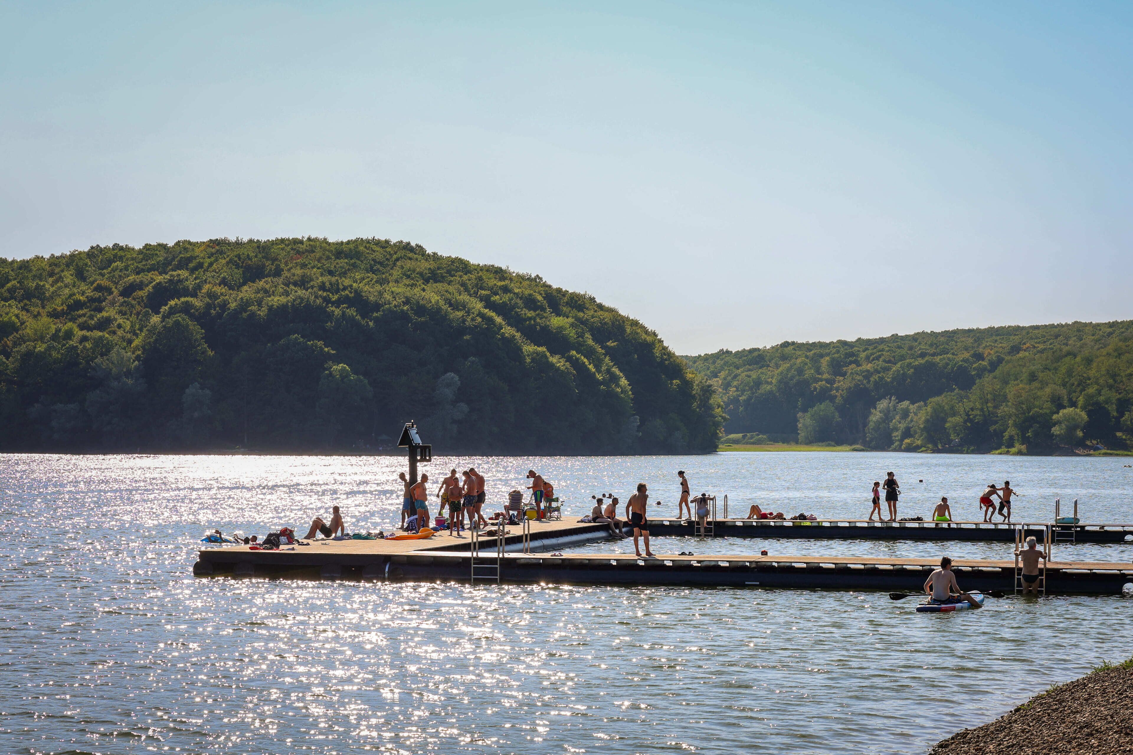 Une jetée au bord du lac où des personnes pratiquent diverses activités, le tout entouré d’une végétation luxuriante.