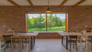 Zona pranzo con pareti in mattoni, travi in legno e un'ampia finestra vista su un paesaggio verde.