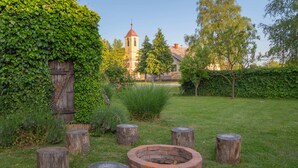 Un giardino con un braciere in mattoni, tronchi di legno e una chiesa sullo sfondo.