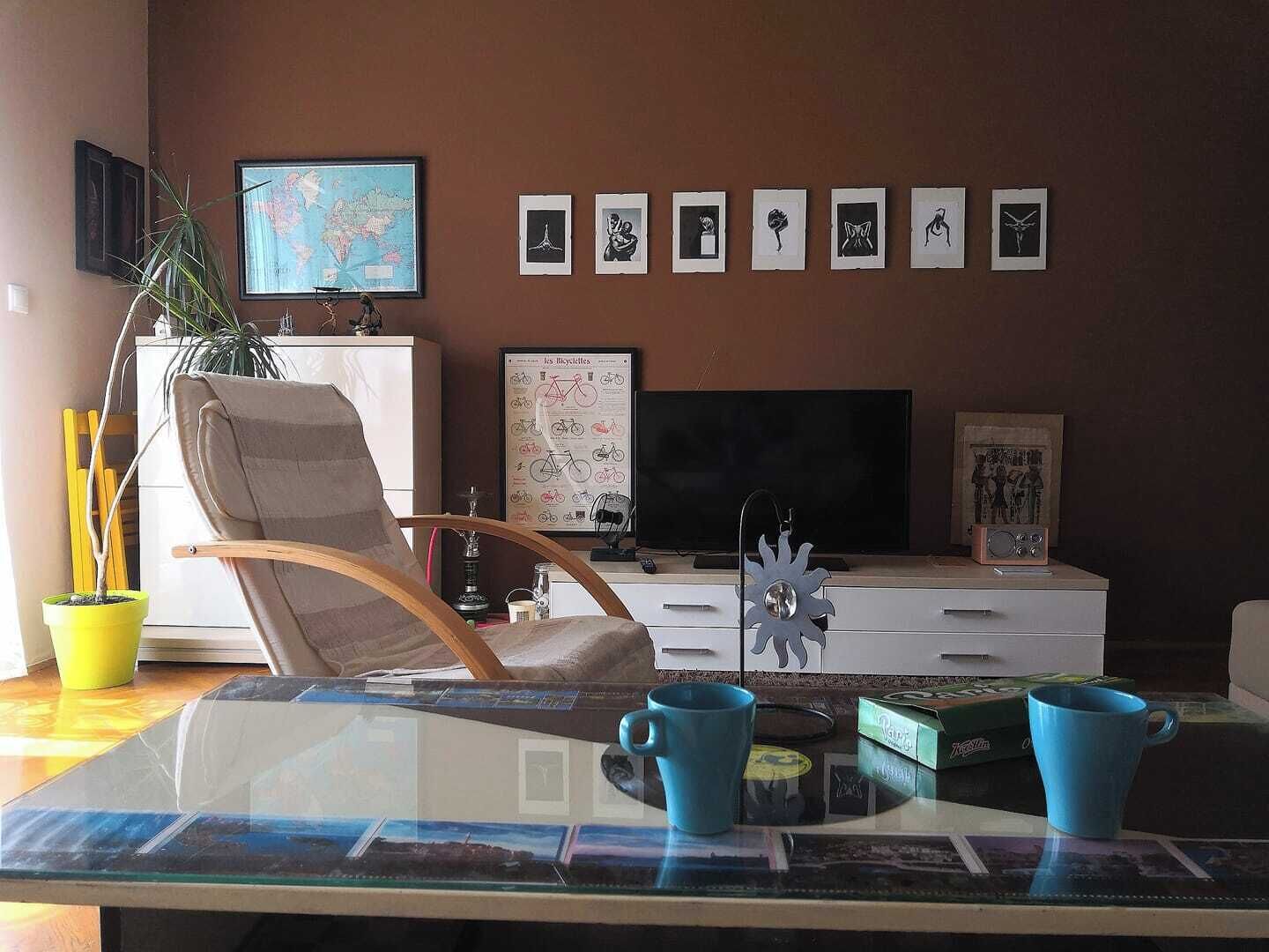 A living room with a TV, framed pictures, a potted plant, and a glass coffee table.