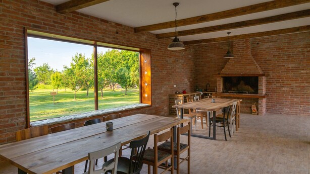 Un'area pranzo rustica con pareti in mattoni, ampie finestre e un camino in muratura.
