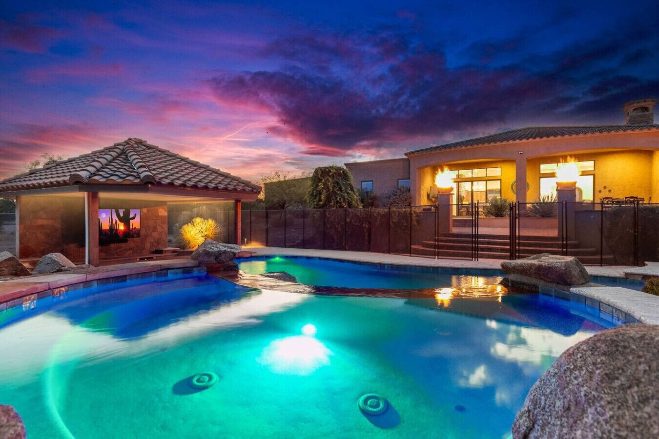 Ein Schwimmbad mit Whirlpool, eine überdachte Terrasse und ein Haus mit beleuchtetem Eingang.