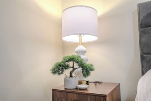 Una mesita de noche con una lámpara, un pequeño árbol en maceta y un objeto decorativo.
