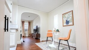 Un pasillo con piso de madera, un área de comedor con dos sillas y una mesa, un televisor y un cuadro en la pared.