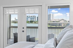 A room with a bed, a view of a balcony with a railing, and a door with a view of buildings and a body of water. - Huge Private Beach☀️ Lakeview Master | Tennis | 5 Pools, 3 Heated☀️ Seascape Resort (Miramar Beach)