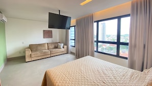 Una habitación de hotel moderna con cama, sofá, televisión de pantalla plana y un ventanal con vista a la ciudad.