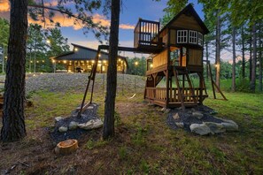 Une cabane en bois dotée d’une terrasse et d’un bâtiment séparé éclairé.