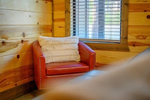 Ein Holzblock-Interieur mit einem roten Ledersessel, einem Fenster mit Jalousien und einer Holzwand.