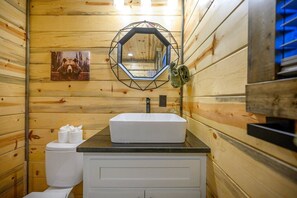 Ein Badezimmer einer Holzhütte mit einem weißen Waschbecken, einem Spiegel und einer Toilette.