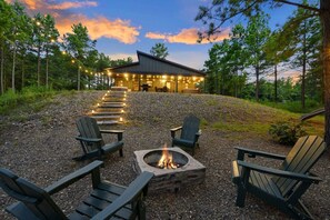 Un chalet doté d’un foyer et de fauteuils Adirondack, situé dans un cadre forestier.
