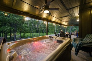 A hot tub with a view of a forest, surrounded by outdoor furniture and a ceiling fan. - The Animal Crossing · Family Cabin w/ Hot Tub & Fire Pit (Broken Bow)