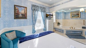 Une chambre à coucher avec un lit, une chaise bleue, une coiffeuse avec une baignoire et un ventilateur de plafond.