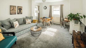 A living room with a sofa, coffee table, dining table, and chairs. There is a clock on the wall and a plant on a stand. - Bright 2BR Home with Private Patio (Greater London)