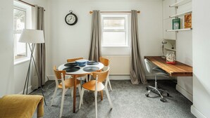 A compact room with a round table, chairs, a clock, a radiator, a desk with a chair, and a bookshelf. - Bright 2BR Home with Private Patio (Greater London)