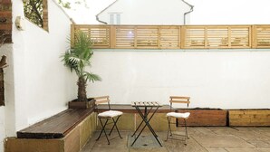 An outdoor patio with a wooden table and two chairs, a potted plant, and a wooden bench. - Bright 2BR Home with Private Patio (Greater London)