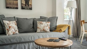 A living room with a grey sofa, patterned cushions, a round coffee table with coasters, a lamp, and a chair. - Bright 2BR Home with Private Patio (Greater London)
