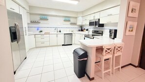 A modern kitchen with white cabinets, a central island, a microwave, and a refrigerator.