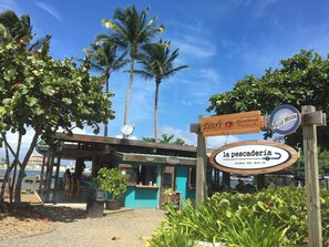 Un restaurant situé en bord de mer, avec une terrasse, une enseigne indiquant « la poissonnerie » et des palmiers en arrière-plan.
