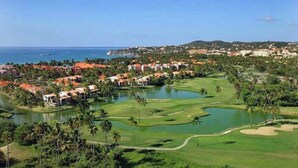 A golf course with a water hazard, surrounded by palm trees and buildings with red roofs.