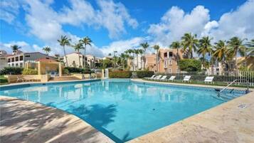 A swimming pool with lounge chairs, palm trees, and buildings in the background.