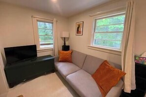 A living room with a sofa, a TV on a stand, a lamp, and windows with curtains. - Acadian Dreams- Entire home next to Acadia (Mount Desert)