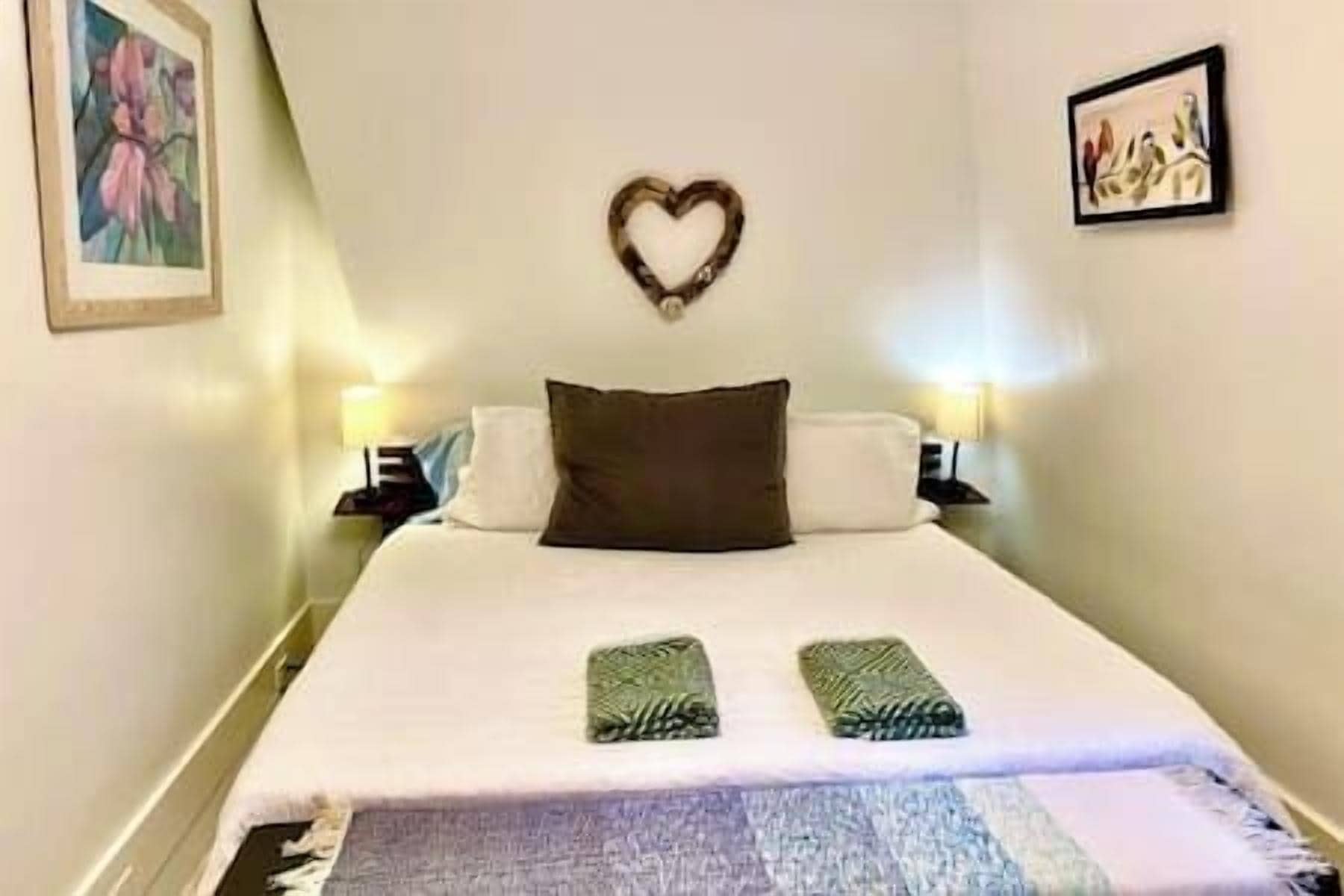 A bed with a heart-shaped decoration, two pillows, a blanket, and a wall-mounted picture.