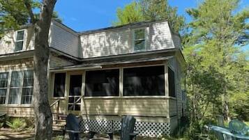 A two-story house with a porch, a visible chimney, and a fenced yard.