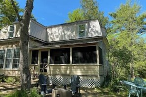 A two-story house with a porch, a visible chimney, and a fenced yard. - Acadian Dreams- Entire home next to Acadia (Mount Desert)