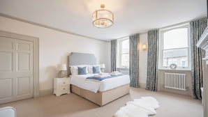 A bedroom with a bed, bedside tables, a lamp, a fur rug, and a view of the outside through a window. - The Lookout, Southwold (Southwold)