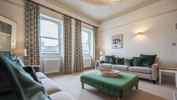 A well-lit living room with a sofa, ottoman, and a lamp. - The Lookout, Southwold (Southwold)