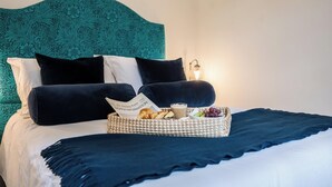 A neatly made bed with a teal patterned headboard, a basket of breakfast items, and a lamp on the bedside table. - The Vault, Southwold (Southwold)