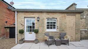 A brick house with a white door, two windows, outdoor seating with cushions, and potted plants. - The Vault, Southwold (Southwold)