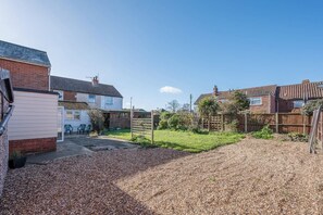 A residential backyard with a gravel driveway, a wooden fence, and a house with a visible garage. - 38 Prospect Place, Leiston (Leiston)