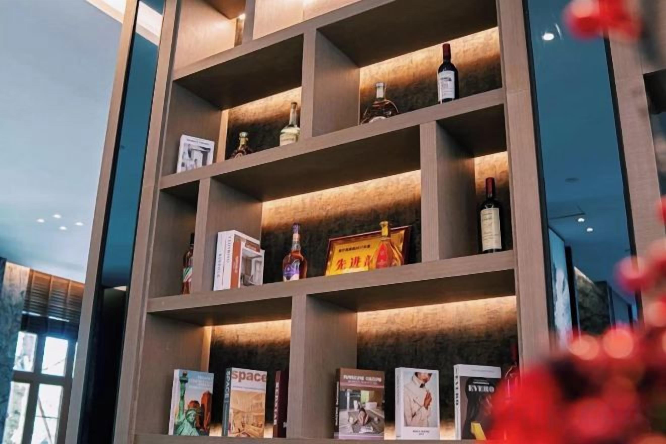 Una estantería con libros y botellas, posiblemente en un hotel o espacio público.