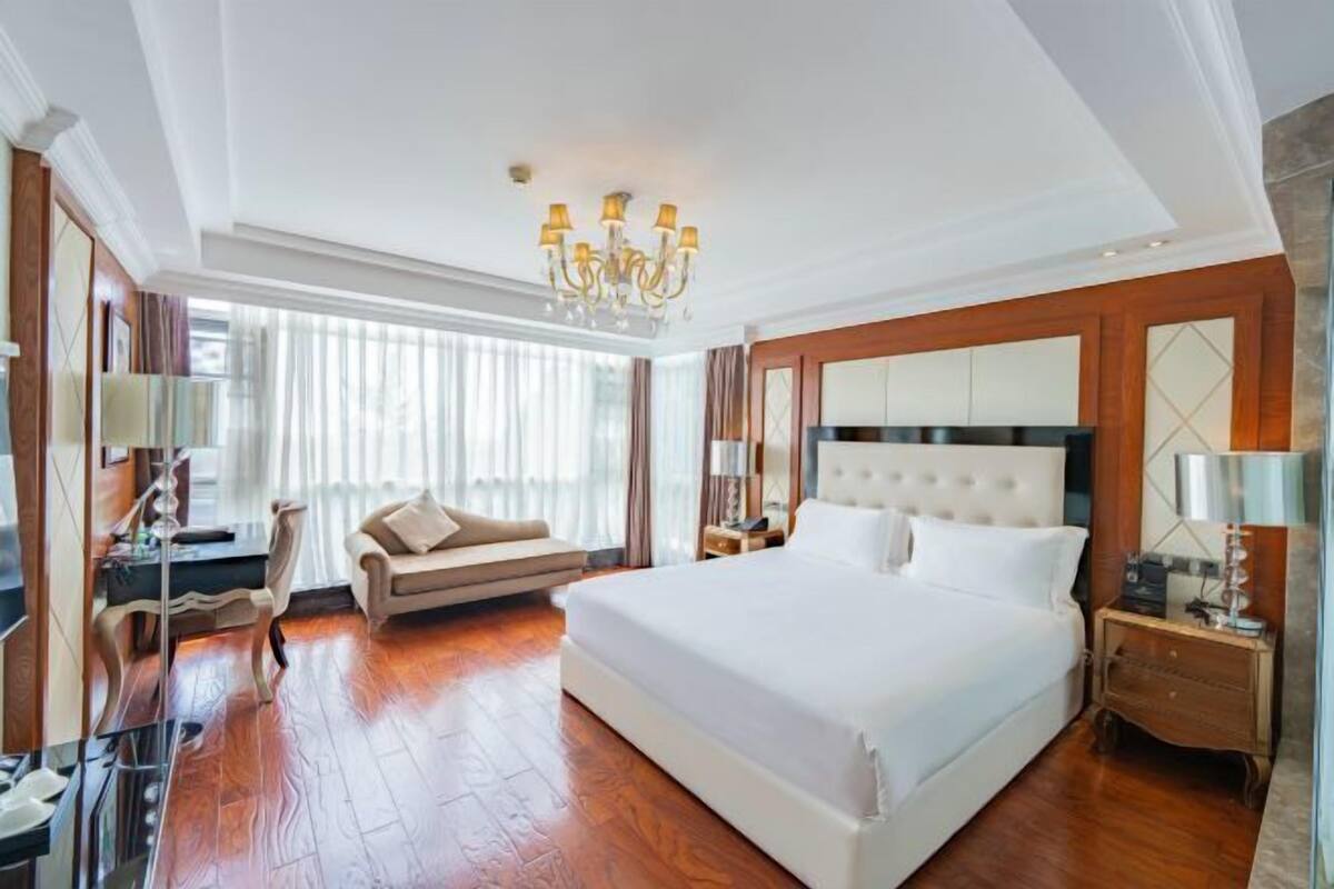 A spacious hotel room with a large bed, a seating area, a desk, and a chandelier.