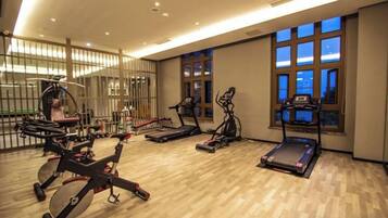 A gym with various exercise equipment, large windows, and a wooden floor.