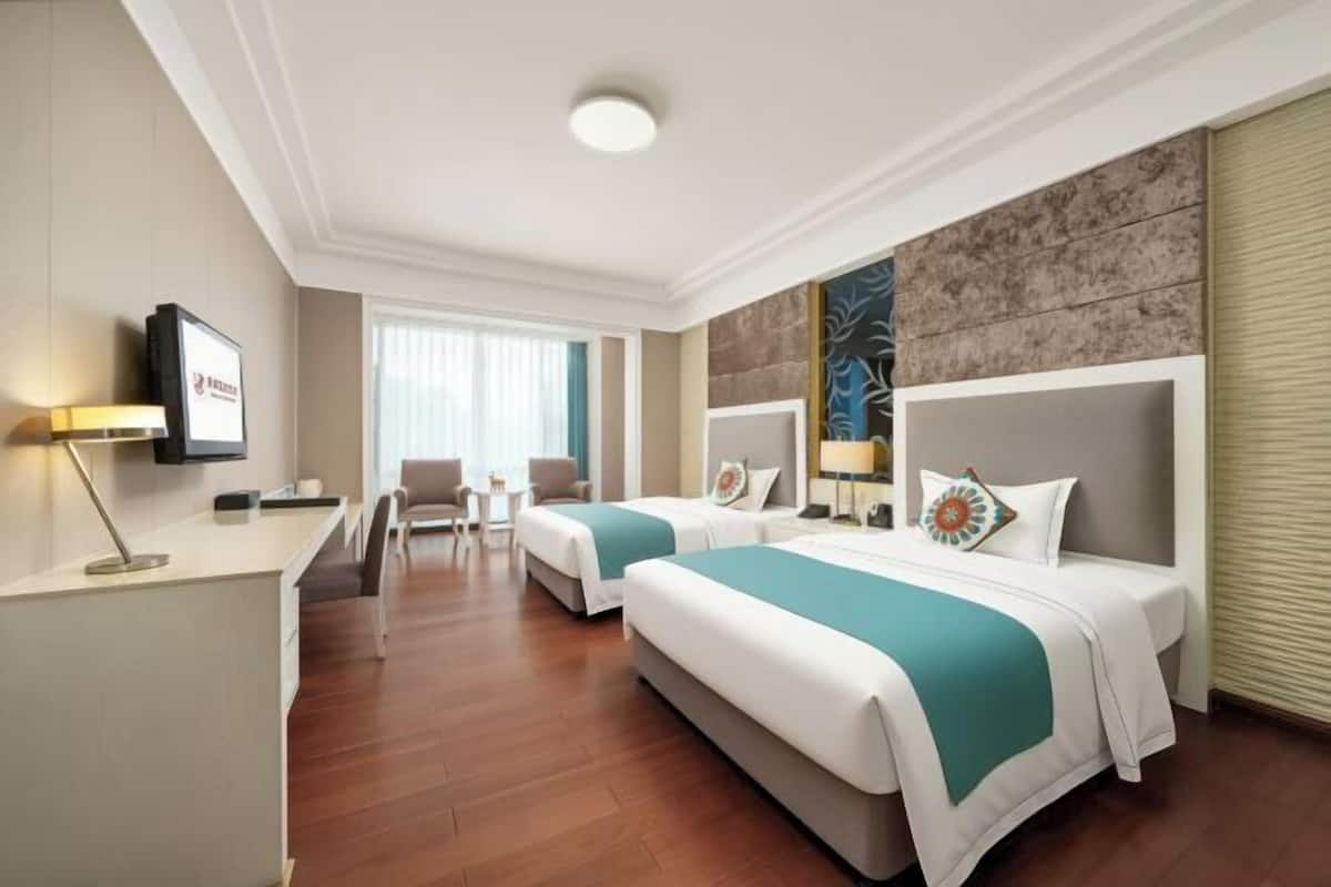 A hotel room with two beds, a desk, a chair, a TV, and a window with curtains.
