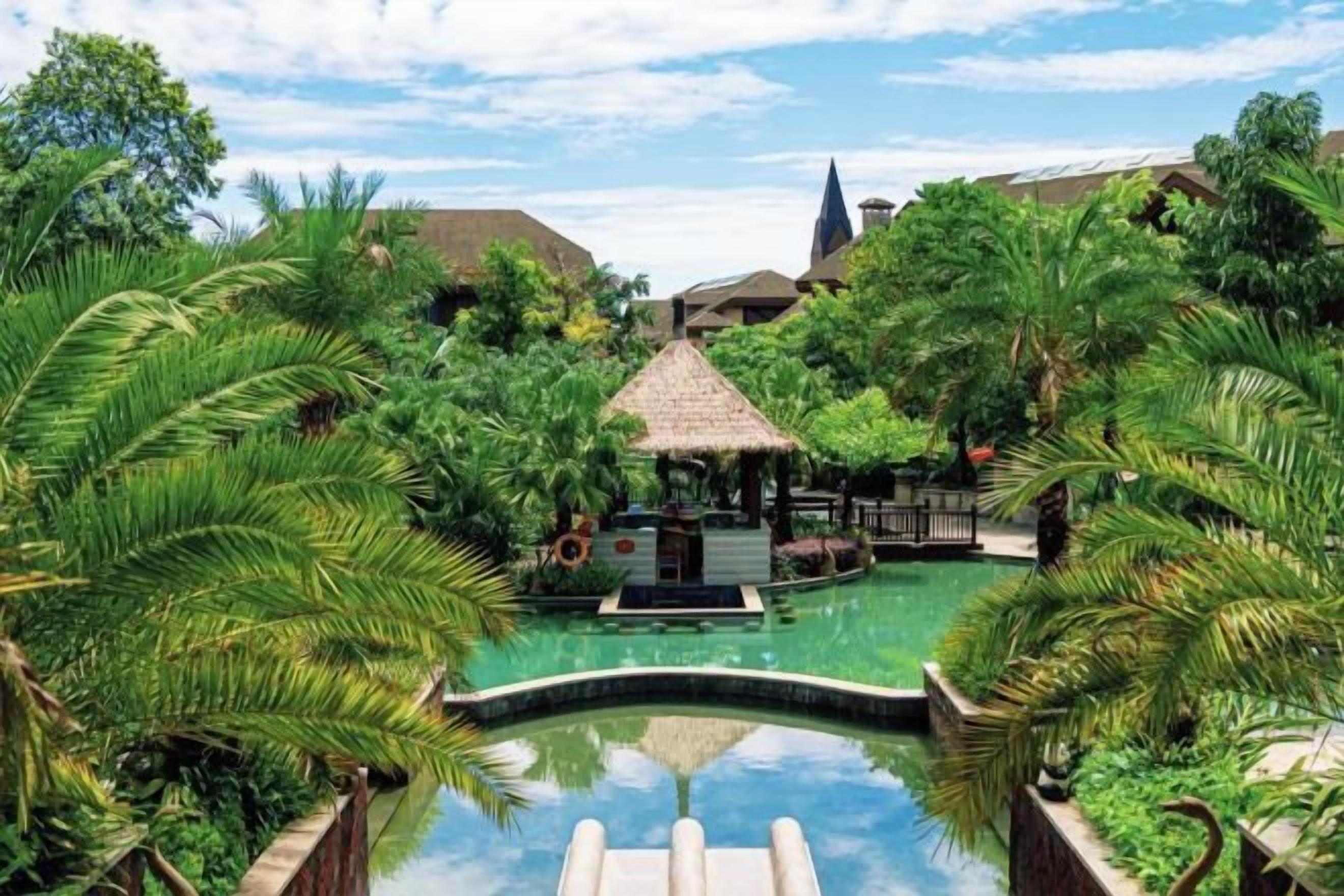 A pool surrounded by lush greenery and a gazebo, with a clear sky above.