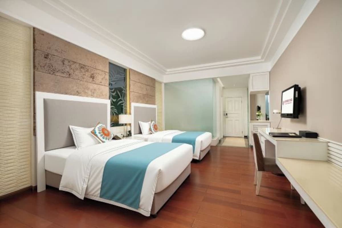 A hotel room with two beds, a desk, a television, and a door leading to another room.