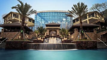 Ein Hotel mit einem zentralen Glasgebäude, einem Pool mit Wasserfall und Palmen.