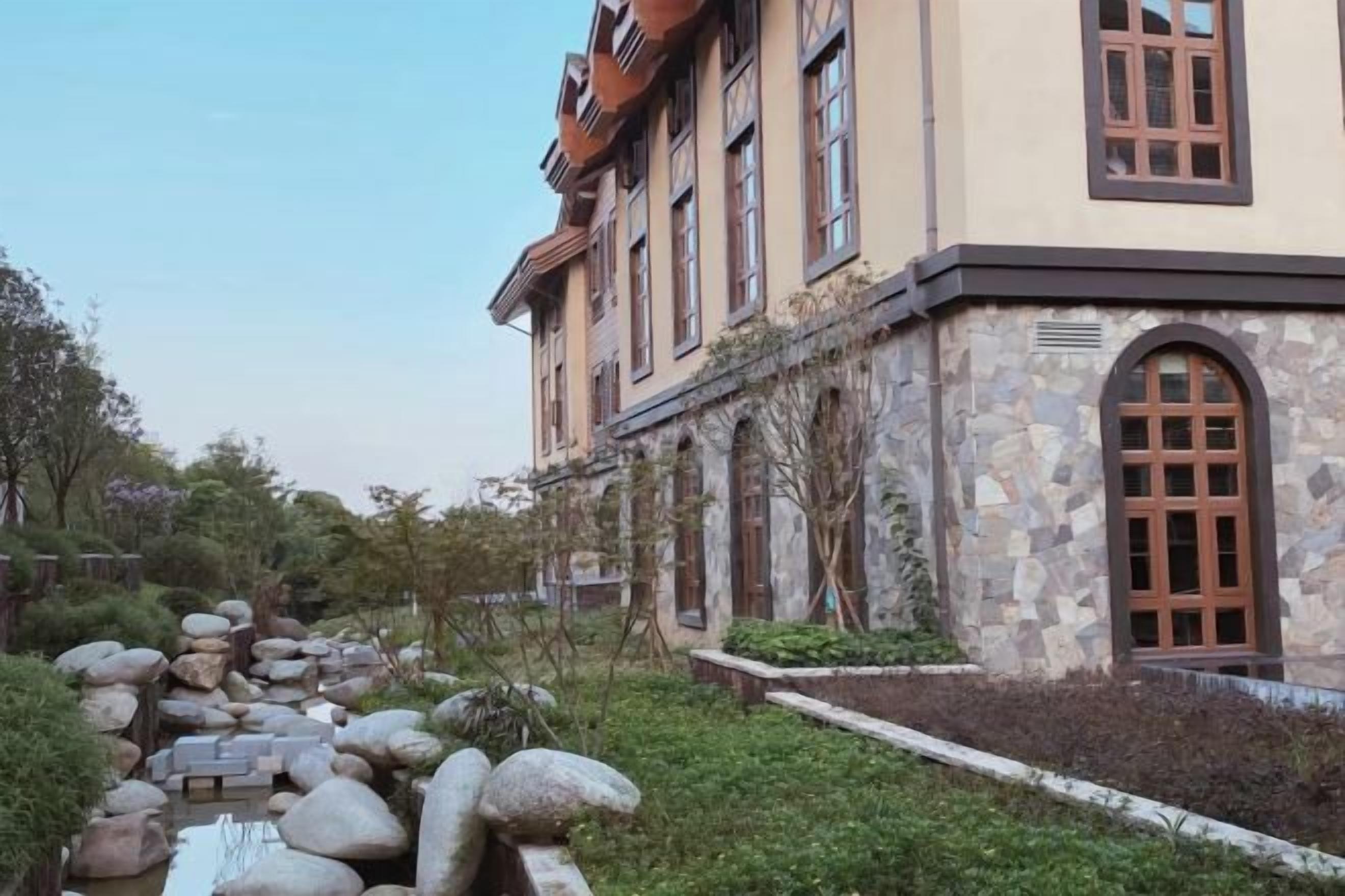 A building with a stone facade, large windows, and a stone pathway leading to a water feature.