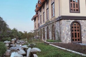 Un edificio con facciata in pietra, ampie finestre e un vialetto in pietra che conduce a un elemento decorativo con acqua.