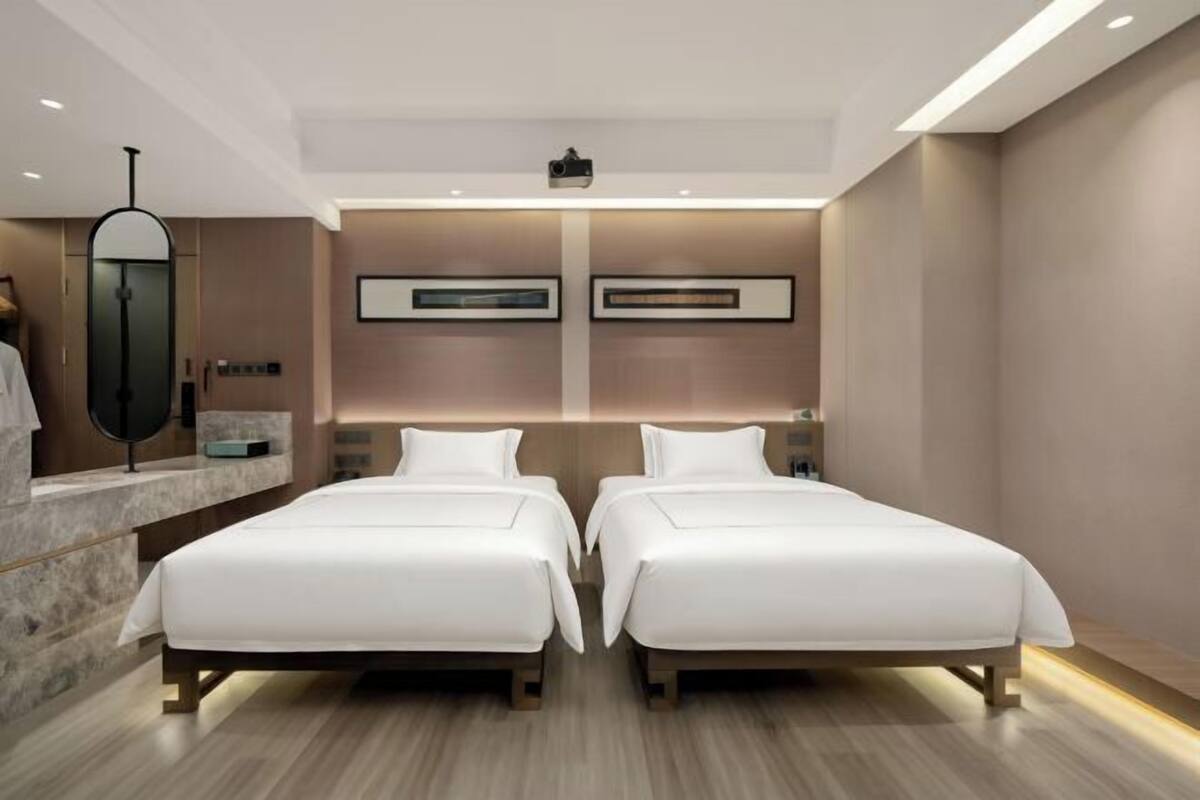 A modern hotel room with two beds, a large mirror, and a minimalist design.