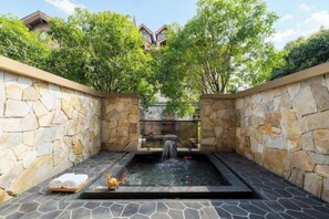 A spa area with a stone wall, a small waterfall, and a pool.