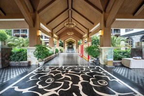 A covered walkway with a patterned floor, wooden ceiling beams, and potted plants.