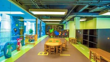 A children's play area with tables and chairs, a large mural, and a window with a view.