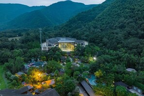 Un grande edificio a più piani immerso nel verde, probabilmente un hotel o un resort, con diversi livelli visibili e un ingresso ben illuminato.