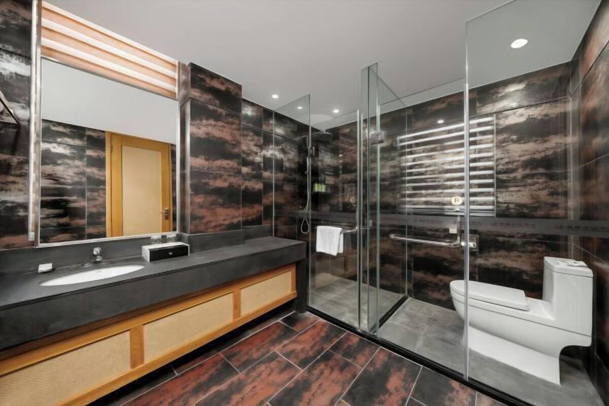 A modern bathroom with a glass shower enclosure, a large mirror, and a dark tiled floor.