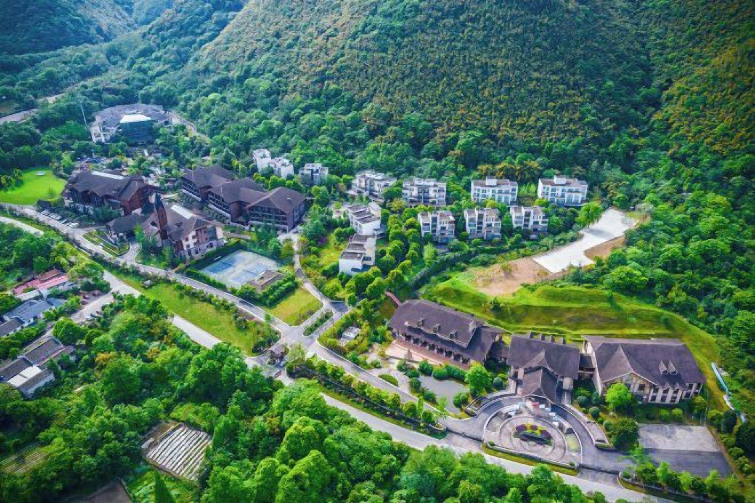 An aerial view of a resort with multiple buildings, a central circular driveway, and surrounding lush greenery.
